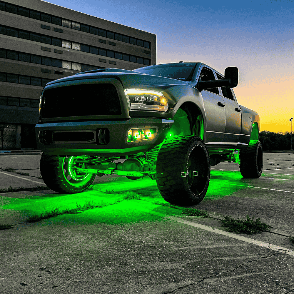 Silver pickup truck with green underglow lights in a parking lot at dusk.